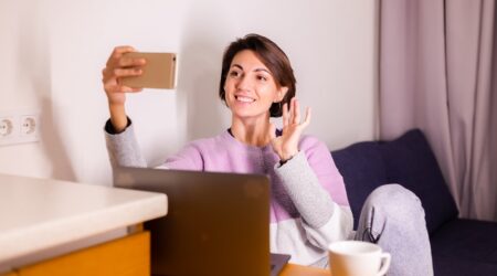 Young caucasian girl woman in bedroom on sofa look at mobile phone  camera